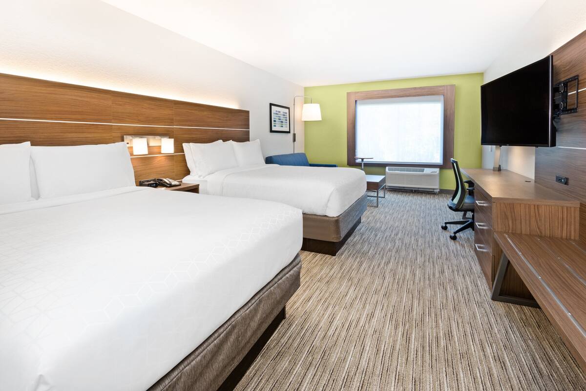 A hotel room with two beds, a desk, a chair, a TV, and a window.