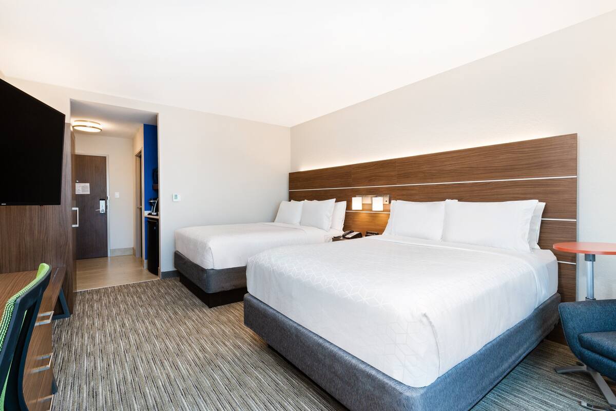 A hotel room with two beds, a desk, a chair, and a TV.