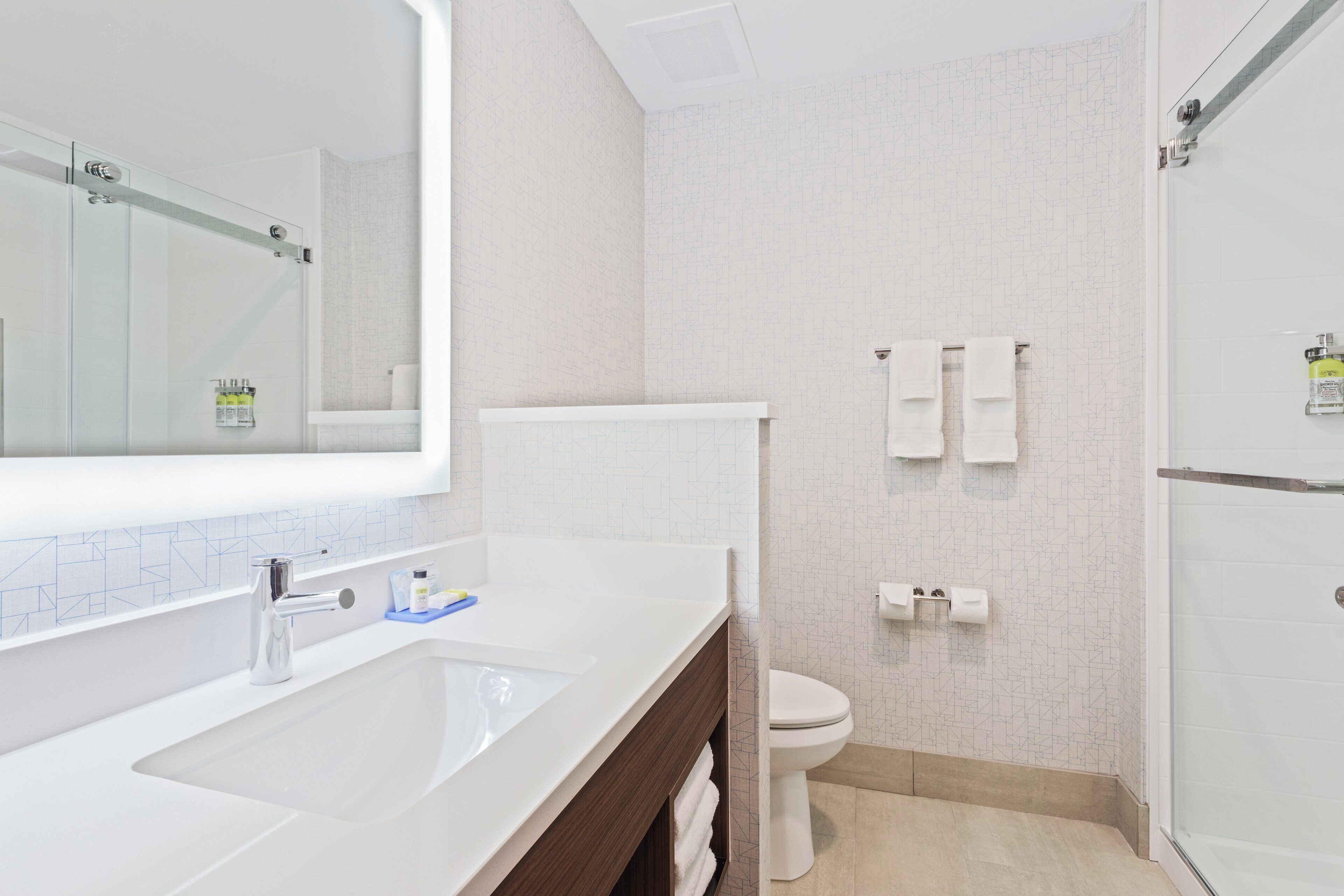 Een moderne badkamer met een grote spiegel, een wastafel, een toilet en een douchegedeelte.