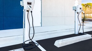 Two electric vehicle charging stations with cables connected to them, set against a building with a blue and white facade. - Holiday Inn Express & Suites Niceville - Eglin Area by IHG (Niceville)
