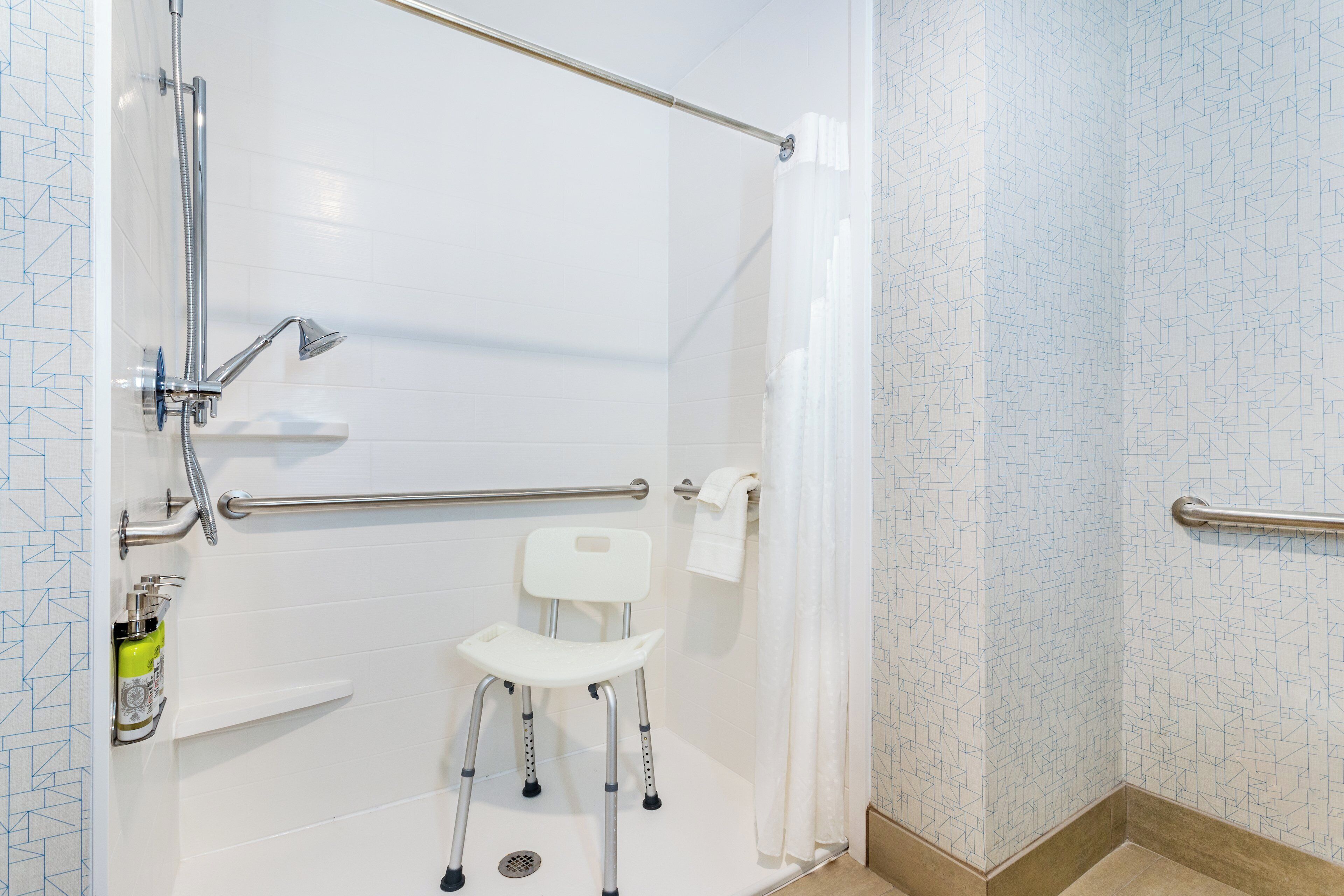 Een douchegedeelte met een handgreep, een witte stoel en een toilet.