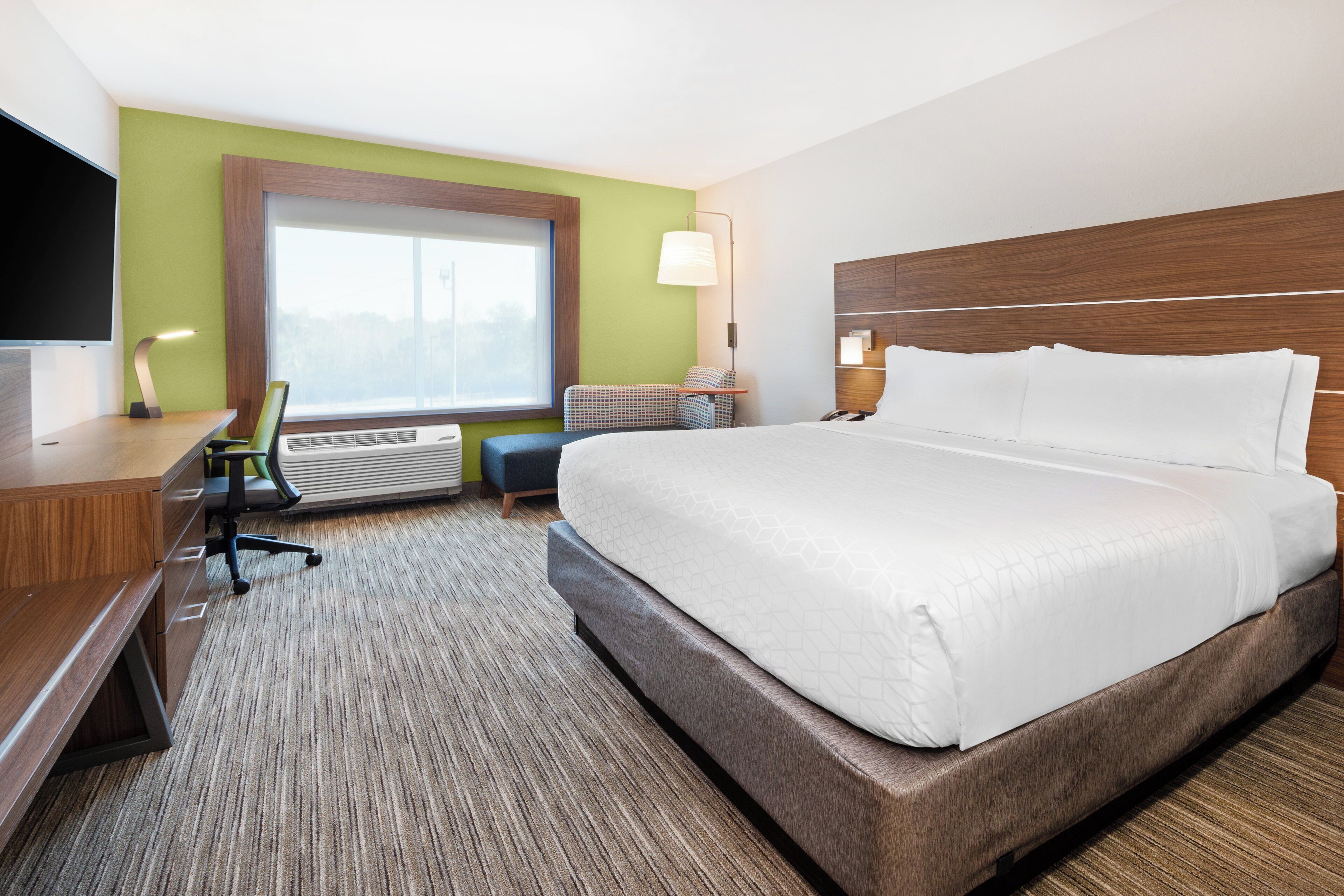 A hotel room with a large bed, a desk, a chair, a television, and a window.