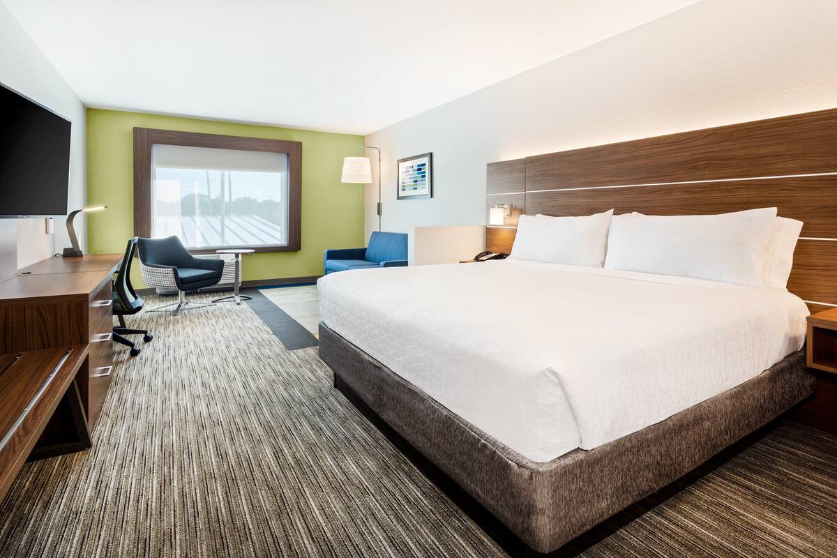 A hotel room with a large bed, a desk, a chair, a TV, and a window with a view.