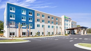 A modern hotel with a blue and beige facade, a covered entrance, and palm trees in front. - Holiday Inn Express & Suites Niceville - Eglin Area by IHG (Niceville)