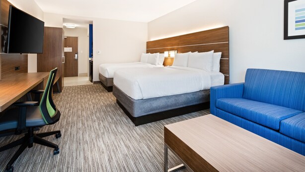 A hotel room with a bed, a blue sofa, a desk with a chair, and a TV mounted on the wall. - Holiday Inn Express & Suites Niceville - Eglin Area by IHG (Niceville)