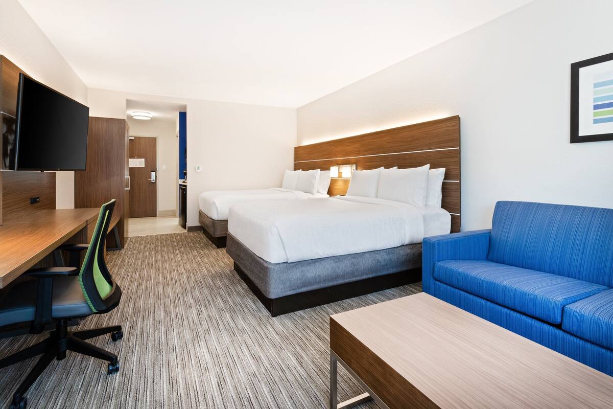 A hotel room with a bed, a blue sofa, a desk with a chair, and a TV mounted on the wall.