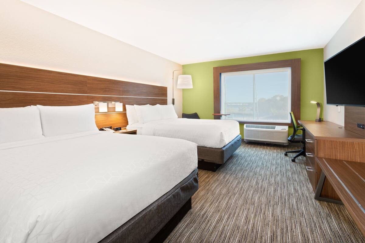 A hotel room with two beds, a desk, a TV, and a window with a view.