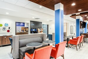 A modern cafe with a seating area featuring a sofa and tables, a coffee station, and a wall with a coffee advertisement. - Holiday Inn Express & Suites Niceville - Eglin Area by IHG (Niceville)