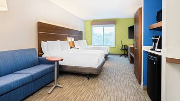 A hotel room with a bed, a sofa, a small table, a desk with a chair, a coffee machine, and a wardrobe.
