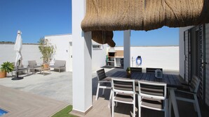 Een terras buiten met een tafel, stoelen, een barbecue en een zwembad.
