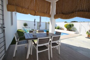 A patio with a table and chairs, a pool, and a white wall with plants. - Private Pool, beautiful and new holiday home casa Manteca in the surroundings of Conil (Conil de la Frontera)