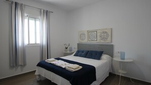 Een slaapkamer met een bed, een raam met gordijnen, een nachtkastje met een lamp en wanddecoratie.