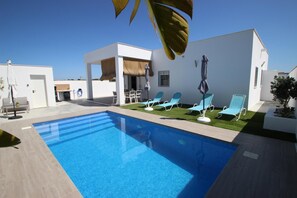 A modern outdoor pool area with a clear blue pool, lounge chairs, and a thatched-roof structure. - Private Pool, beautiful and new  holiday home casa Manteca in the surroundings of Conil (Conil de la Frontera)
