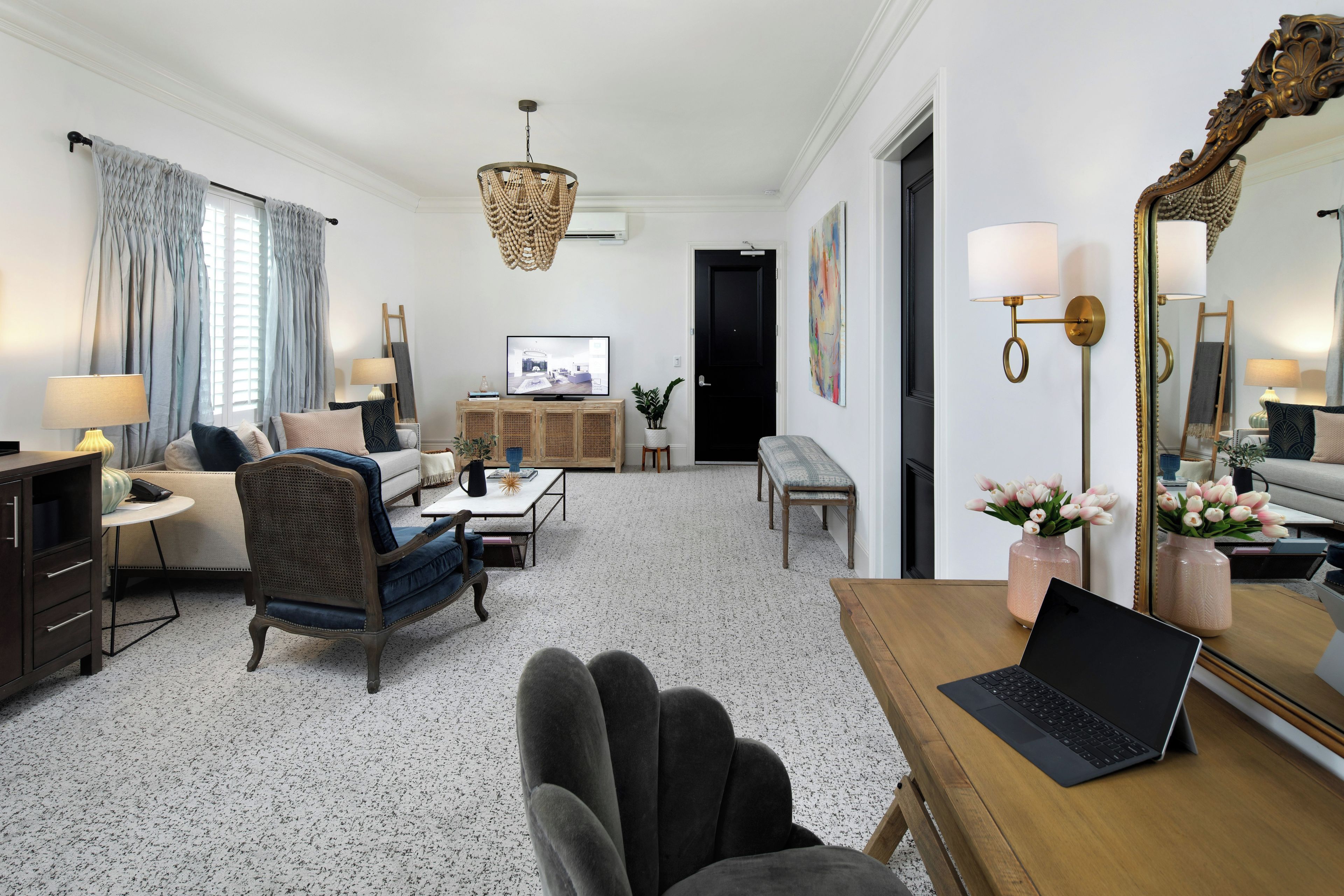 Una sala moderna con sofá, sillones, una mesa de centro y televisor. Hay una computadora portátil sobre una mesa de madera y un espejo en la pared.