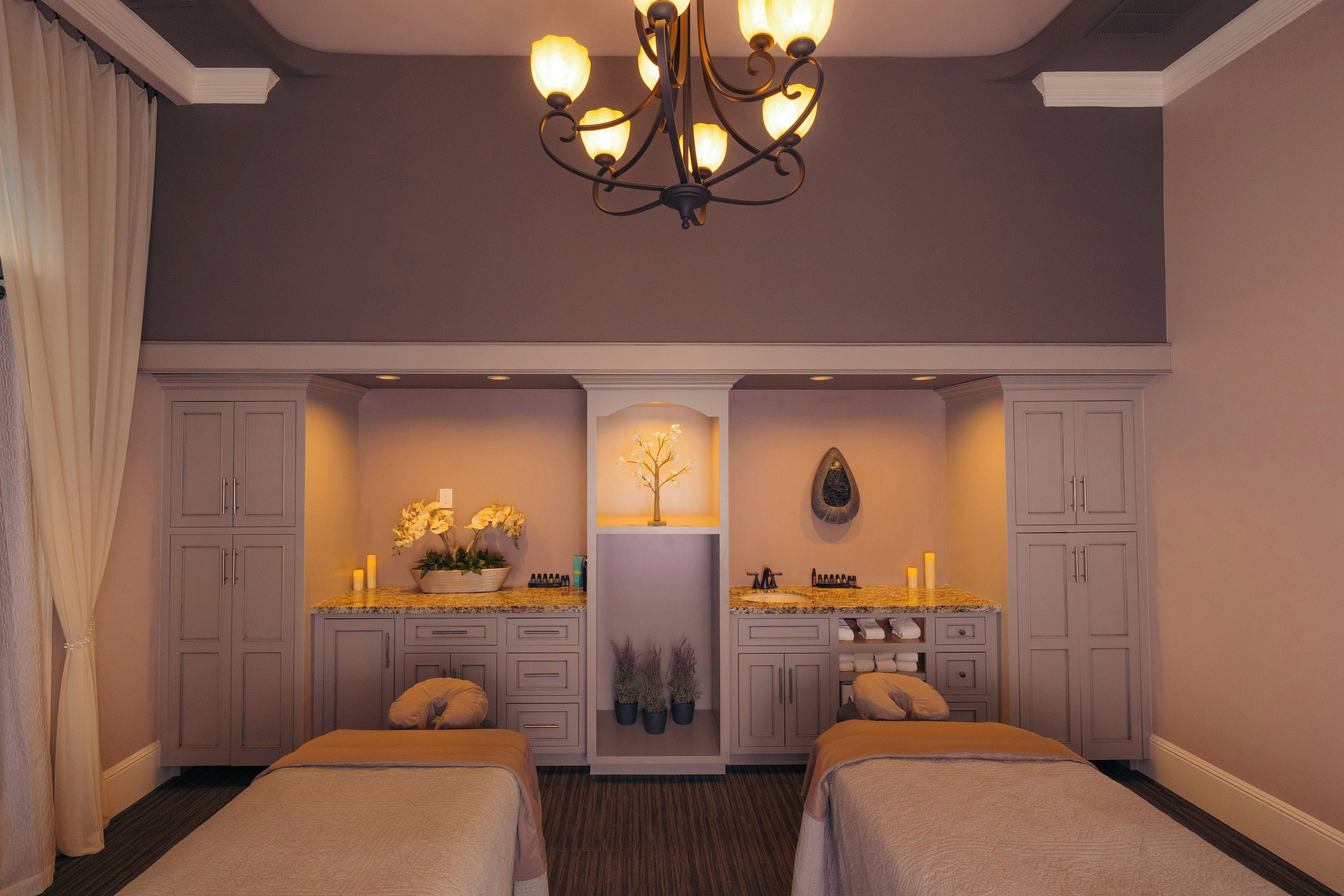 A hotel room with two beds, a chandelier, a vanity with a mirror, and a small tree decoration.