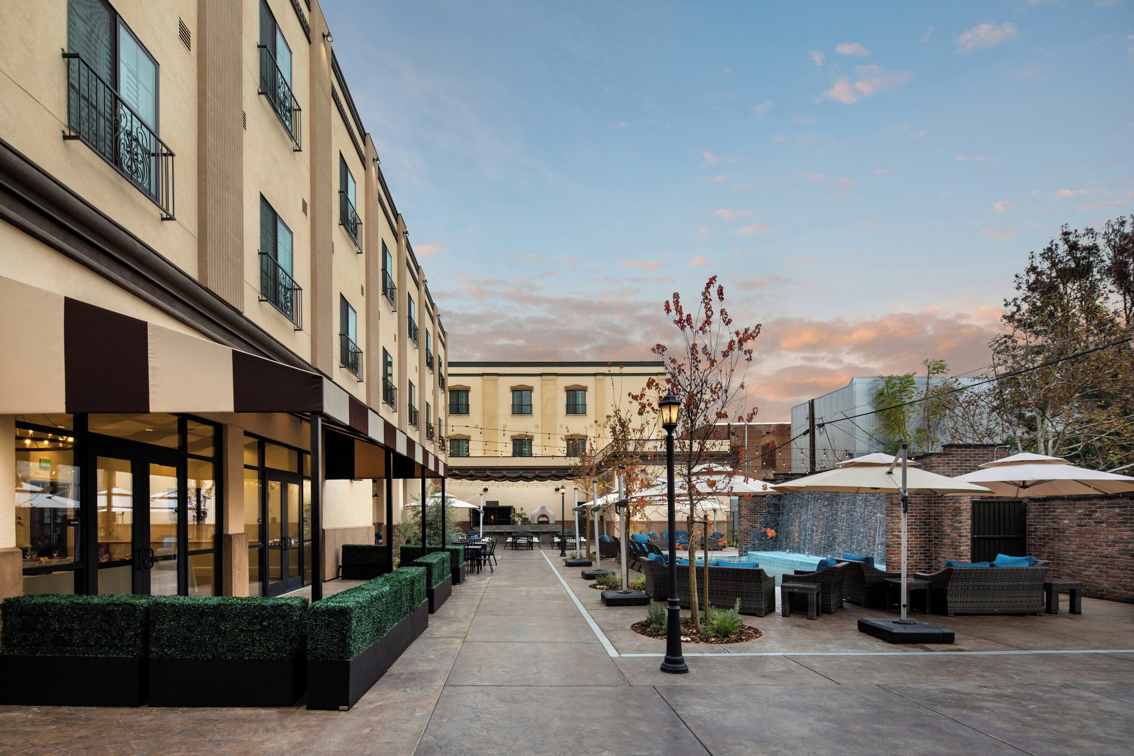 Un patio con mobiliario exterior, una piscina y un edificio con varias ventanas.