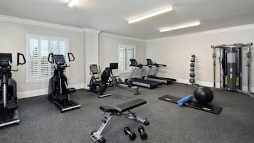 Une salle de sport équipée de tapis de course, de vélos elliptiques, d’un banc de musculation, d’haltères et d’un ballon lesté.