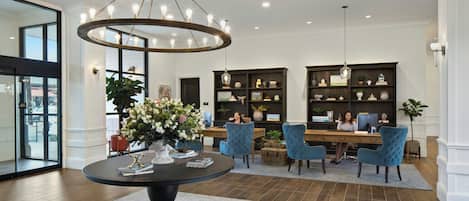 A lobby with a round table, blue chairs, a chandelier, and a reception desk with a computer.