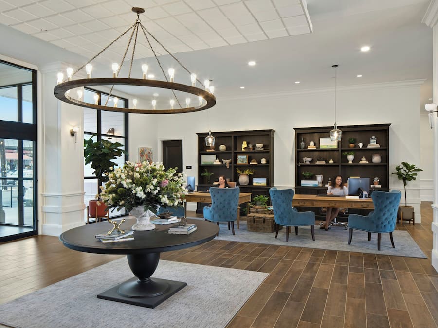 A lobby with a round table, blue chairs, a chandelier, and a reception desk with a computer.