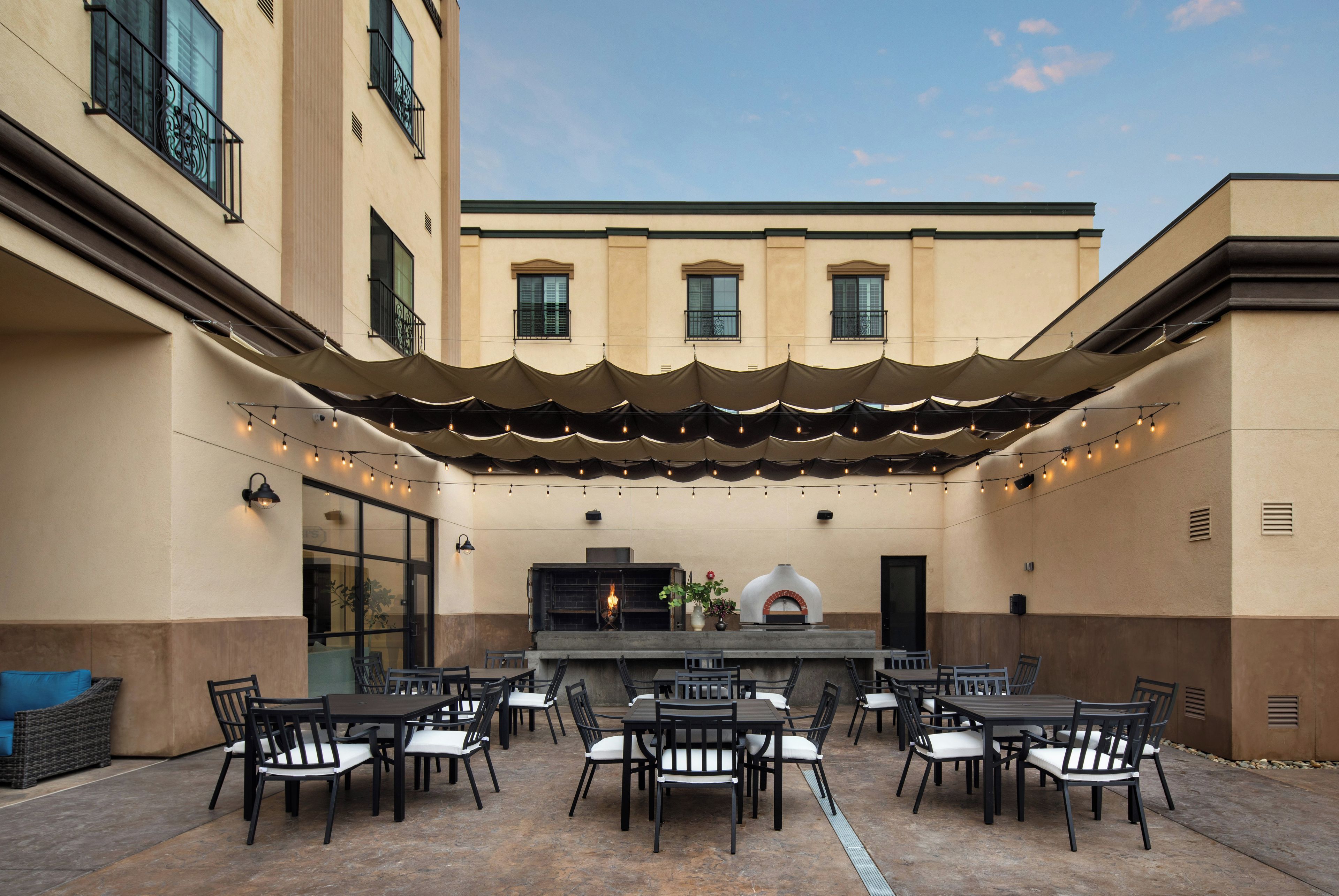 An outdoor patio with a dining area, tables, chairs, and a pizza oven.