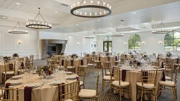 A banquet hall with round tables, gold chairs, and chandeliers.