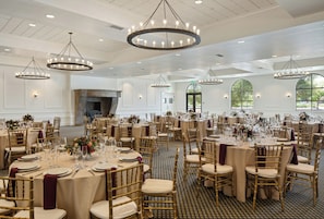 Un salón de banquetes con mesas redondas, sillas doradas y candelabros.