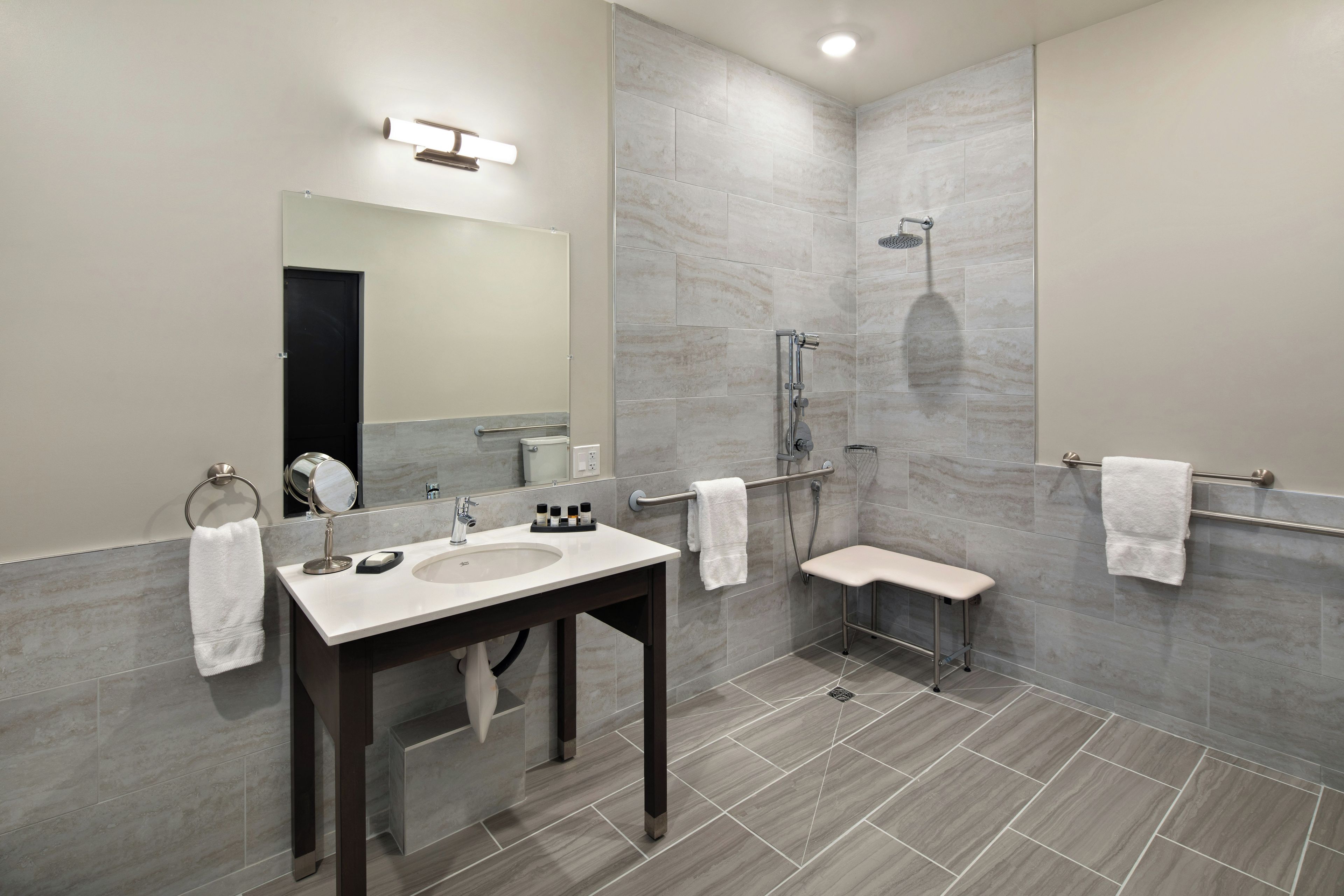 A modern bathroom with a vanity, mirror, shower, and towel racks.