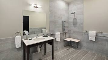 A modern bathroom with a vanity, mirror, shower, and towel racks.
