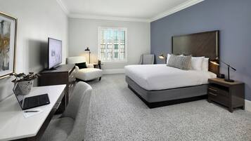 Habitación de hotel con cama, mesitas de noche, un escritorio con computadora, una silla y una ventana con persianas.