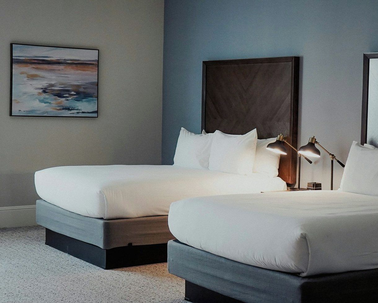 A hotel room with two beds, a large dark headboard, and a painting on the wall.