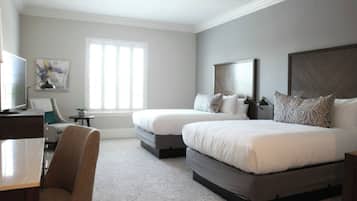 A hotel room with two beds, a desk, a chair, a television, and a window.