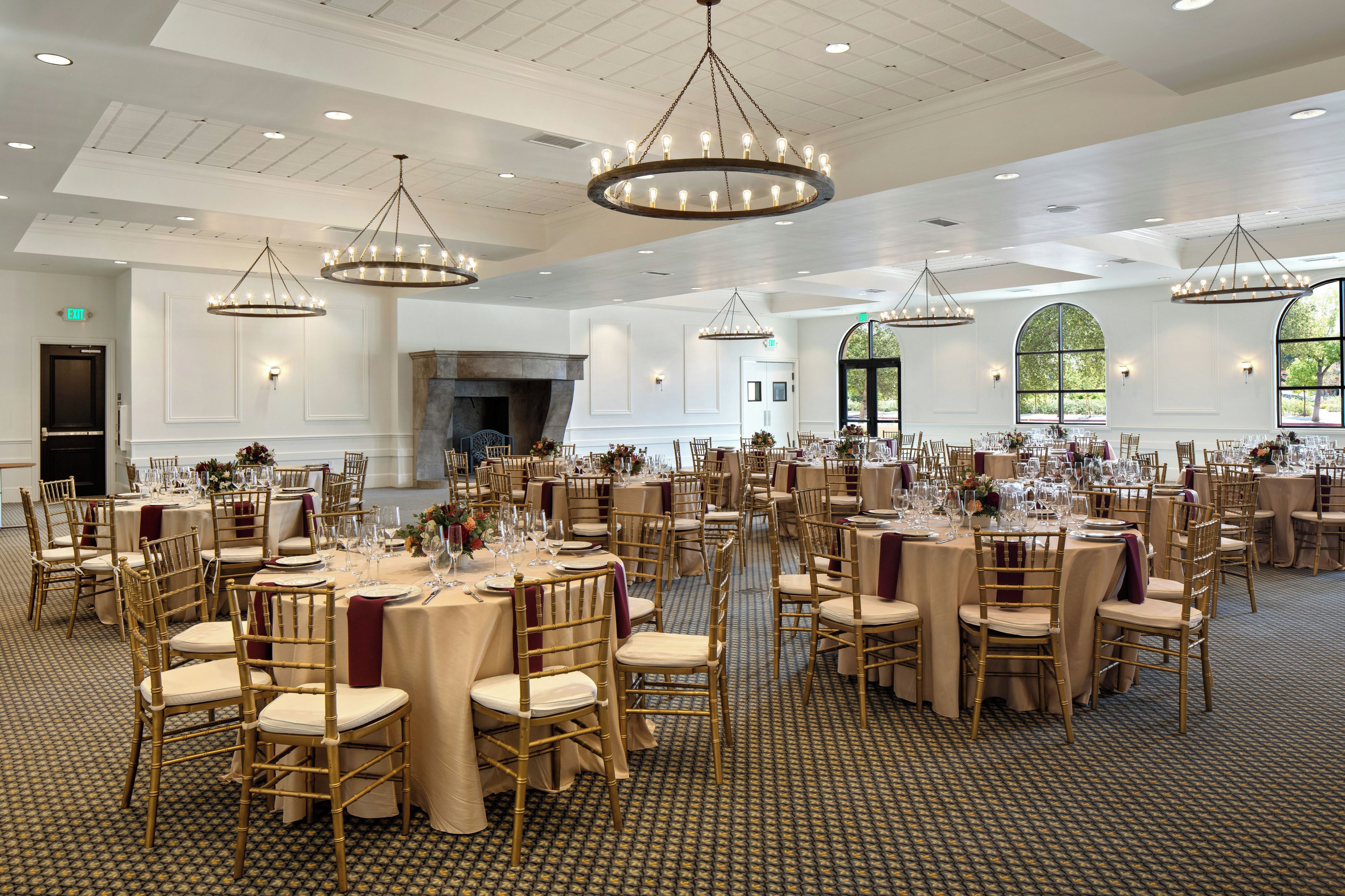 Un amplio salón de banquetes con varias mesas redondas, sillas doradas y elegantes candelabros.
