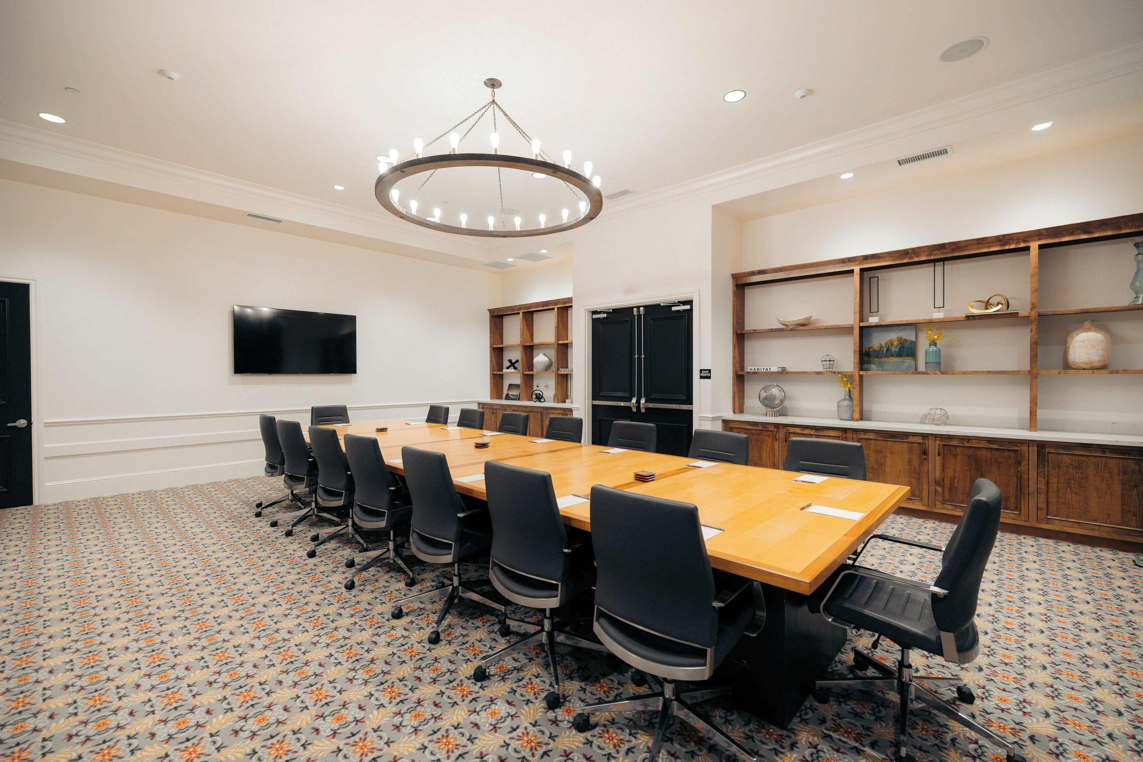 A conference room with a long table, chairs, a flat-screen TV, and a decorative chandelier.