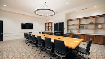 A conference room with a long table, chairs, a flat-screen TV, and a decorative chandelier.