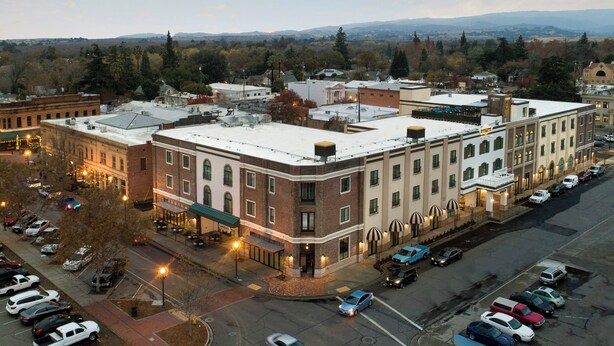 A multi-story building with a flat roof, a parking lot, and a street view. - Hotel Winters (Winters)