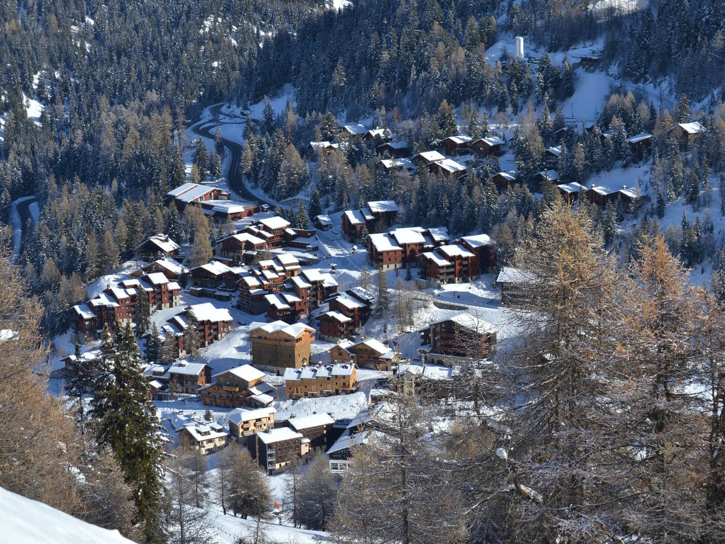 Un pueblo cubierto de nieve en la montaña, con cabañas de madera y una estación de esquí.