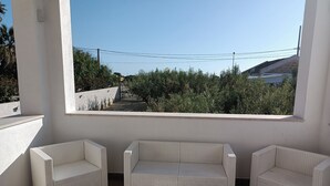 A balcony with white wicker furniture, a view of greenery, and a clear sky. - Signorino Resort Quadruple Studio Apartment (MARSALA)
