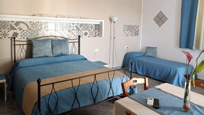 A bedroom with two beds, a table with a vase, and patterned wall tiles. - Signorino Resort Quadruple Studio Apartment (MARSALA)