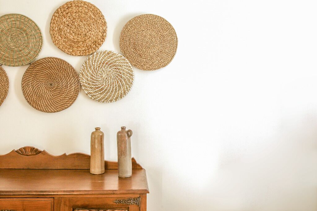A wooden dresser with two ceramic pitchers and several woven coasters on the wall.