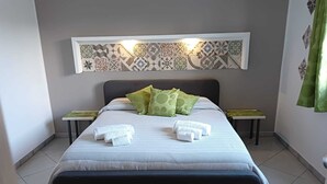Habitación de hotel con cama, almohadas, cabecero, lámpara fijada a la pared, alfombra verde y una pequeña mesa con mantel verde.