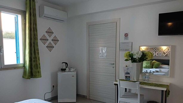 Habitación de hotel con una cama, un escritorio con espejo, un refrigerador pequeño, un televisor y una ventana con cortinas.