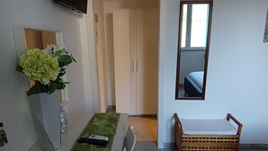 Una habitación con una mesa de comedor, un banco de madera pequeño, un espejo y una puerta que da a otra estancia.
