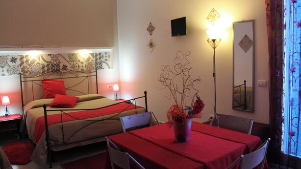 Een hotelkamer met een bed, een tafel met een rode tafelkleed, een stoel, een lamp en een vaas met bloemen.