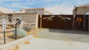 Una entrada con reja, un letrero con número, un cactus y un edificio de diseño moderno.