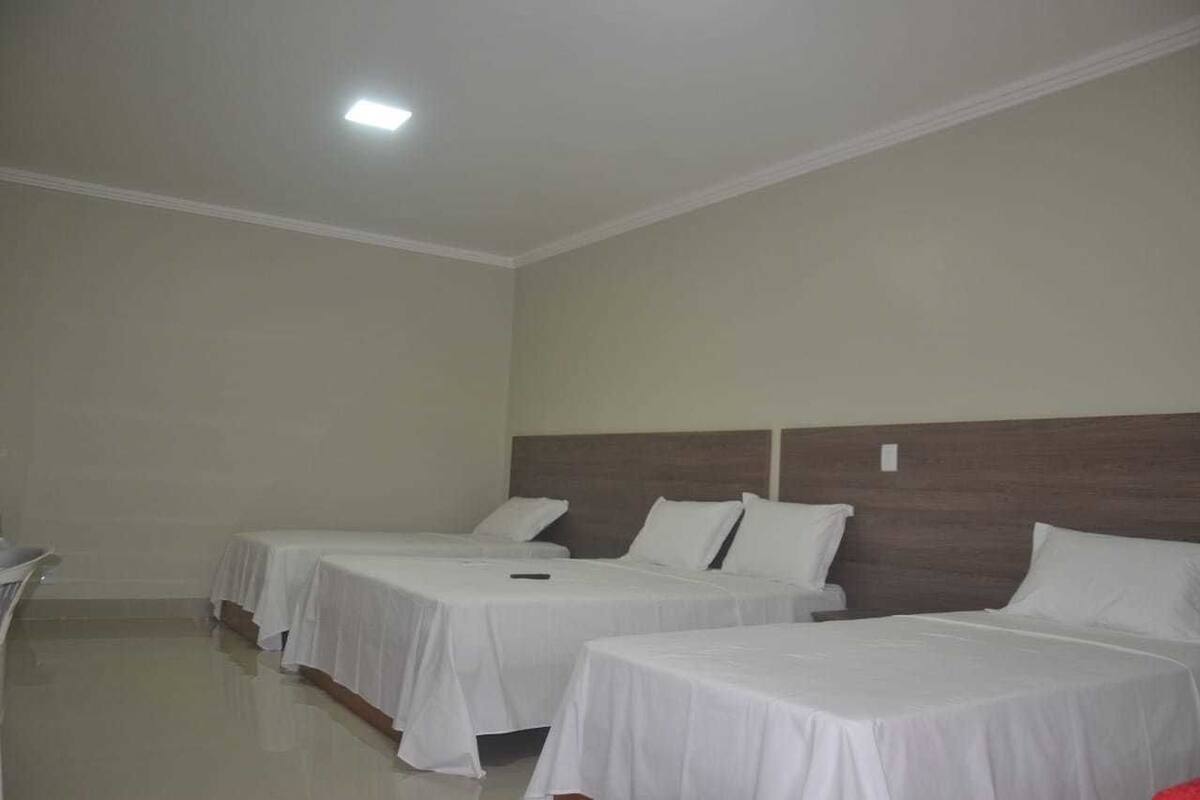 Una habitación de hotel con tres camas individuales, un cabecero de madera y una pared blanca.
