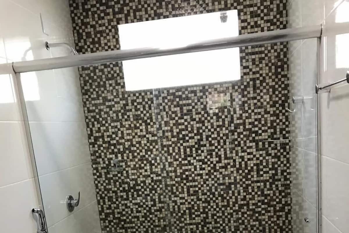 Un baño con inodoro, cabina de ducha con pared de mosaico a cuadros y una toalla en el suelo.