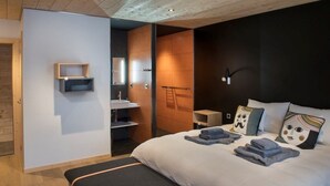 Una habitación de hotel moderna con una cama grande, una mesita de noche, un armario empotrado y un pequeño rincón de descanso.