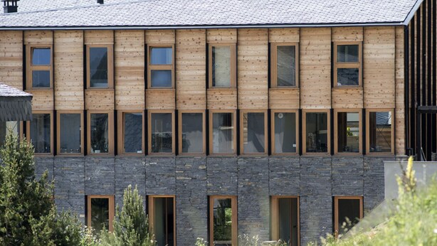 Un edificio moderno con fachada de madera y base de piedra, que cuenta con múltiples ventanas y puertas.