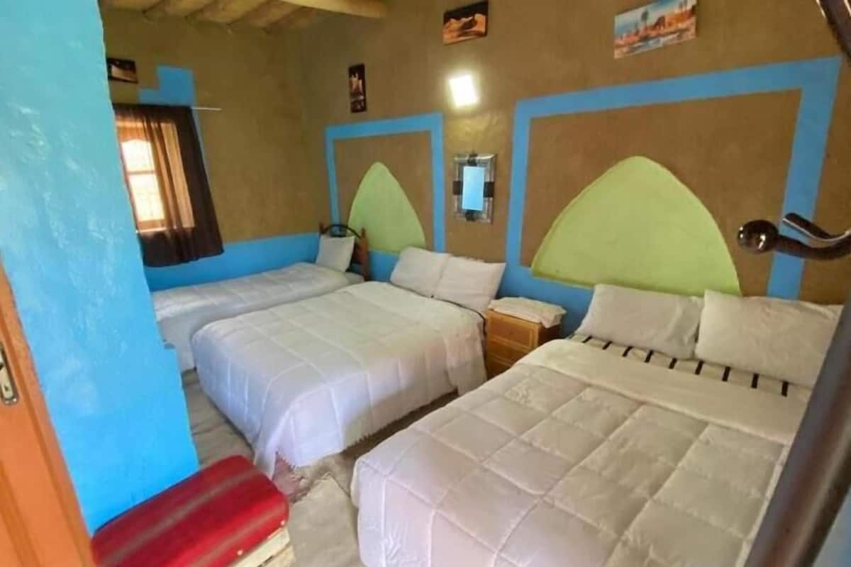 Een kamer met twee bedden, elk met een hoofdeinde, een klein nachtkastje en een raam met gordijnen.