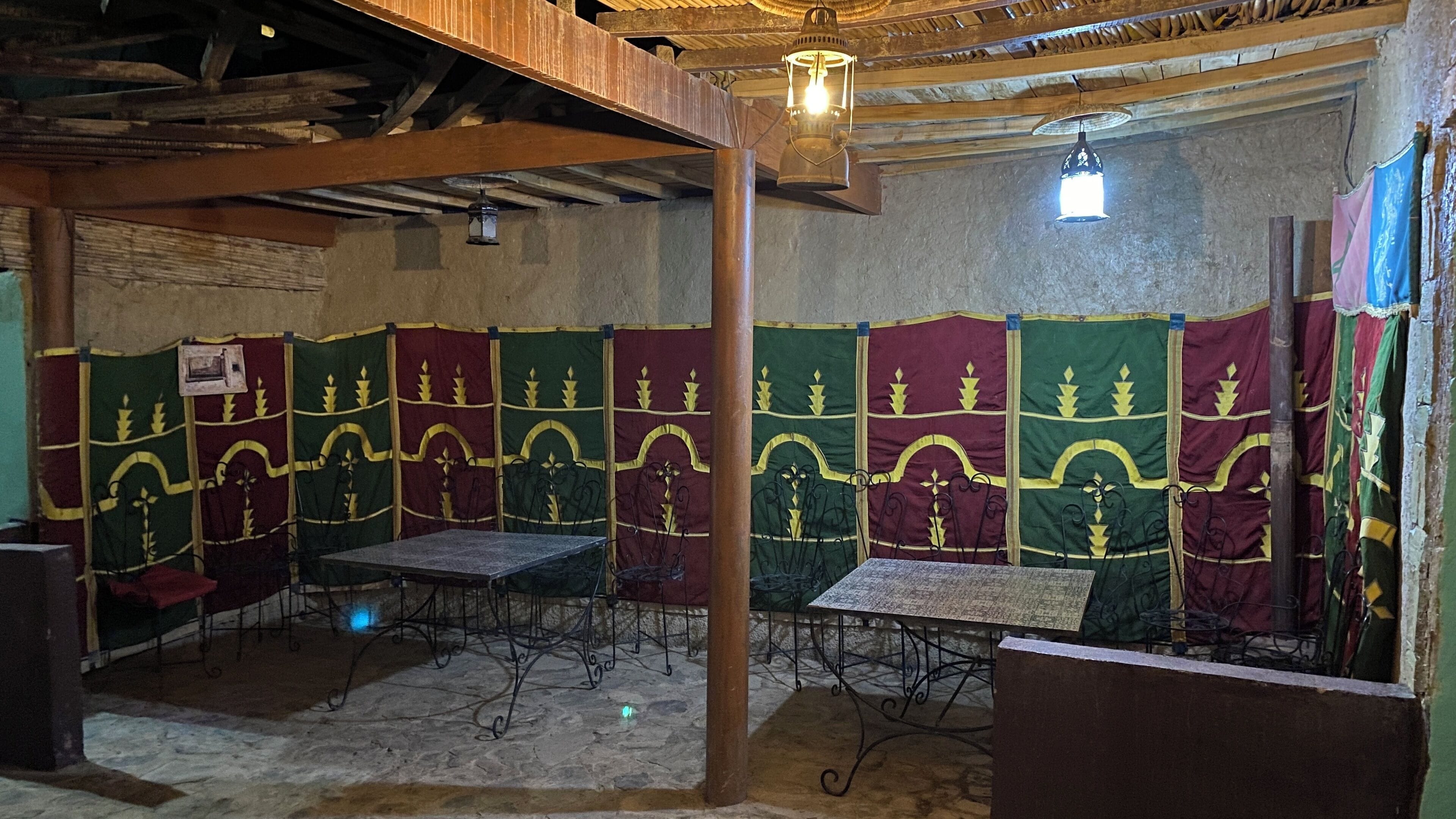 A room with a rustic wooden ceiling and walls, metal tables with chairs, and patterned curtains.